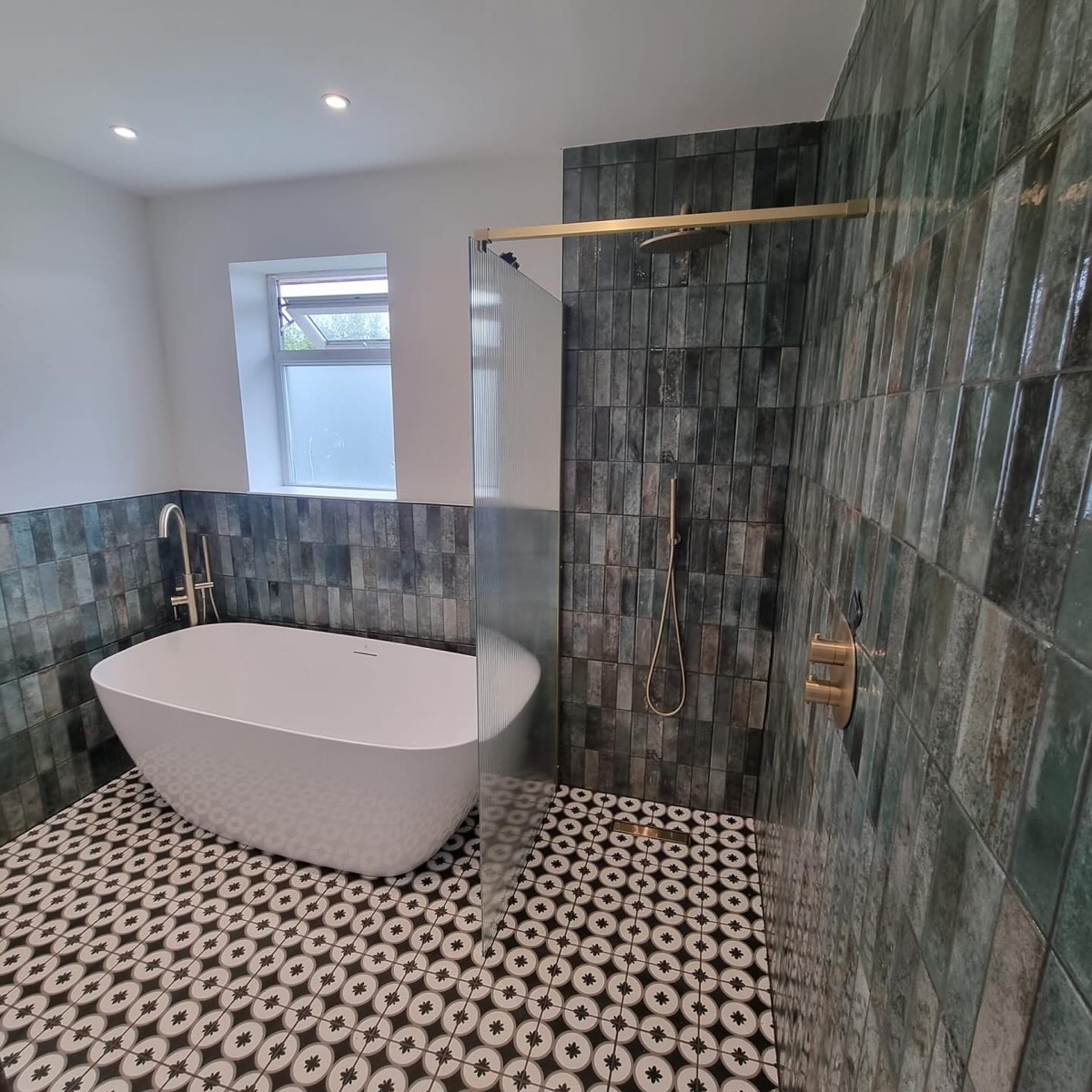 Wet room with freestanding bath, green gloss tiles, patterned floor and brushed brass shower